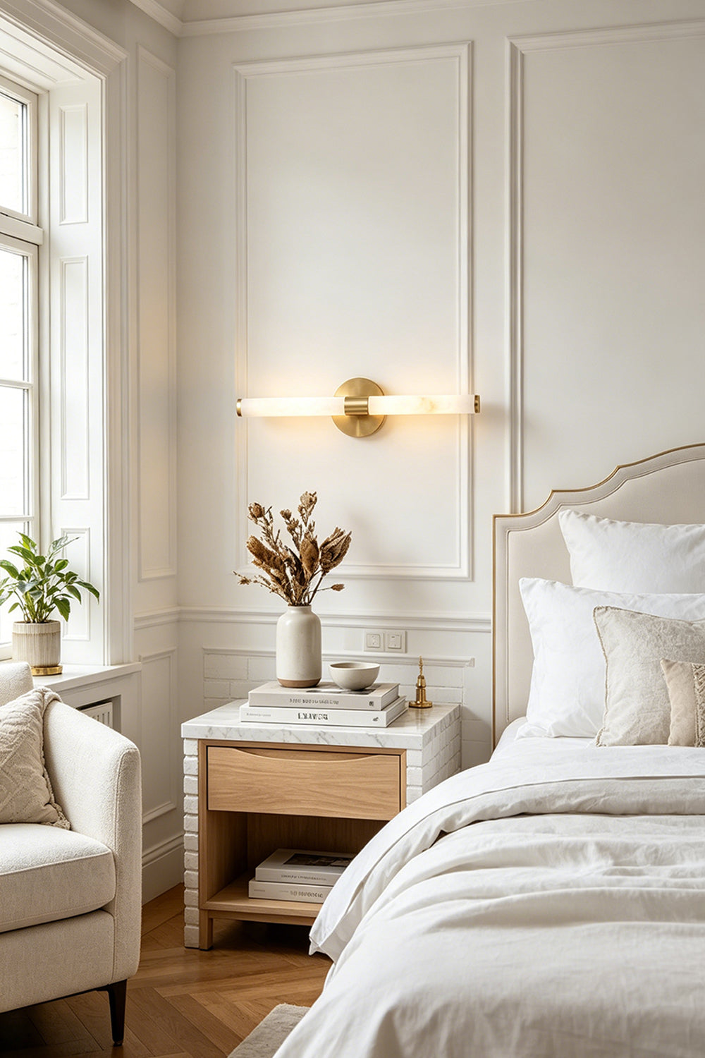 Nerida Linear Alabaster Wall Sconce | Alabaster, Brass | Mounted horizontally as an elegant bedtime light casting a warm golden glow above a wooden nightstand in a classical white bedroom | vexa lamps