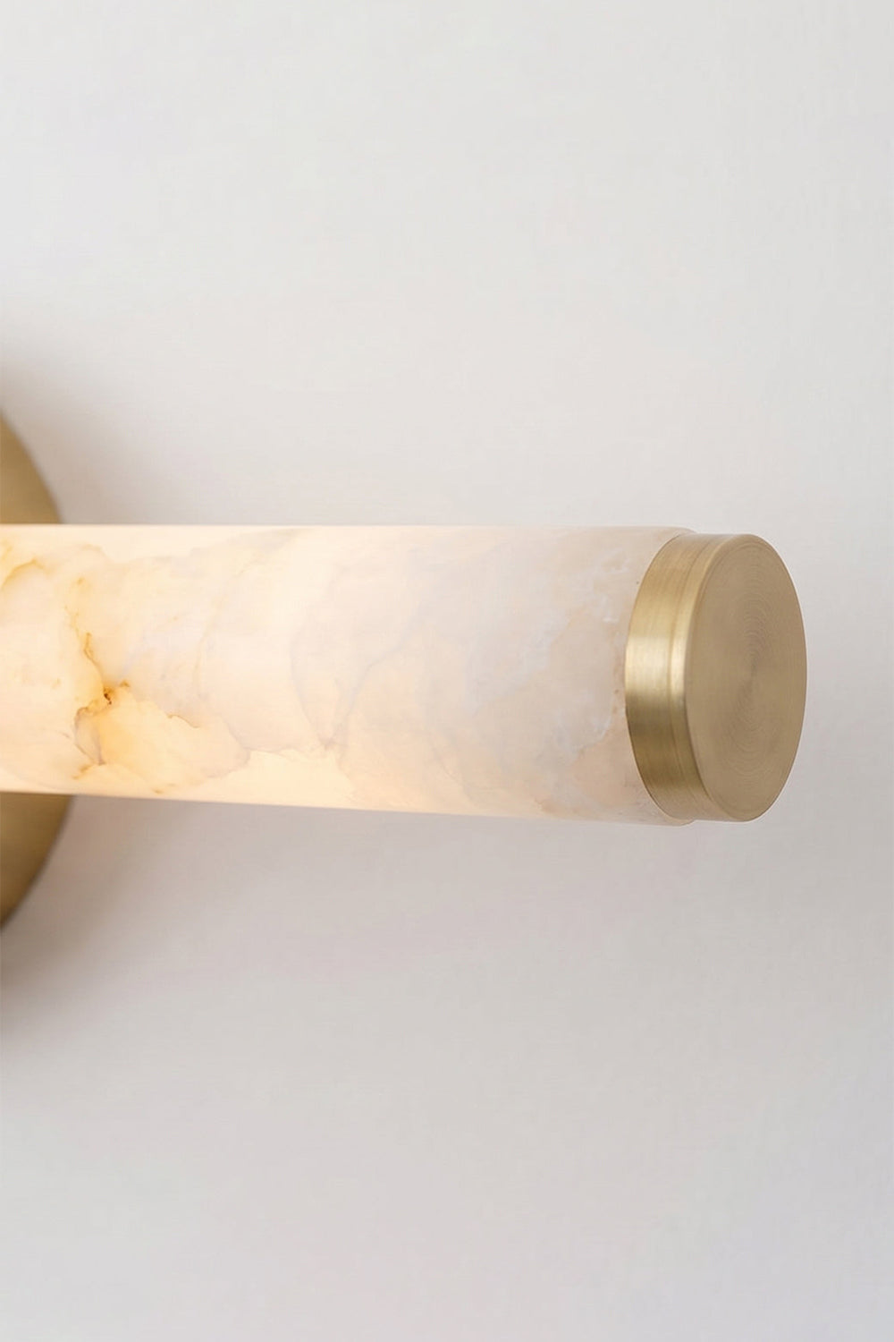 Nerida Linear Alabaster Wall Sconce | Alabaster, Brass | Detailed shot of the illuminated end of the alabaster tube showcasing a translucent soft warm glow and the matching gold brass cap | Detail shot | vexa lamps