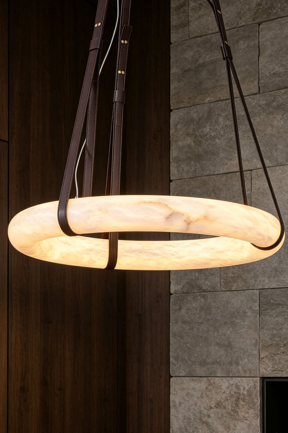 Nerissa Alabaster Ring Leather Pendant Light | Natural Alabaster, Leather and Brass | Close view of the 3-strap ring pendant hanging near a dark wood wall | vexa lamps