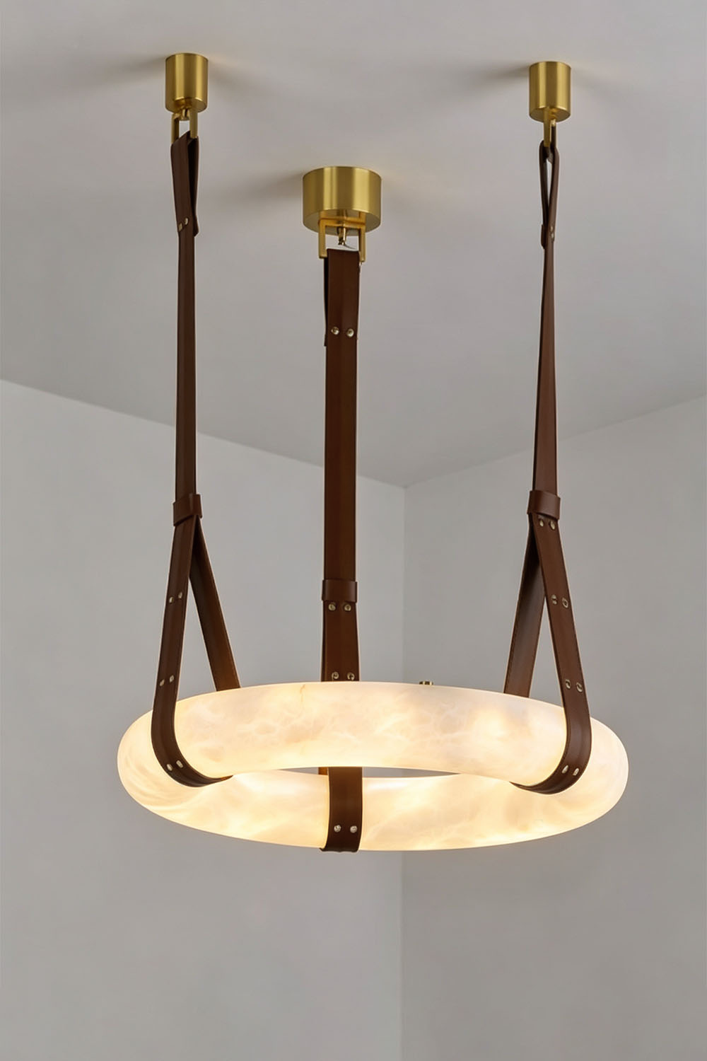 Nerissa Alabaster Ring Leather Pendant Light | Natural Alabaster, Leather and Brass | Studio shot of 3-strap ring variant illuminated on a neutral wall | vexa lamps