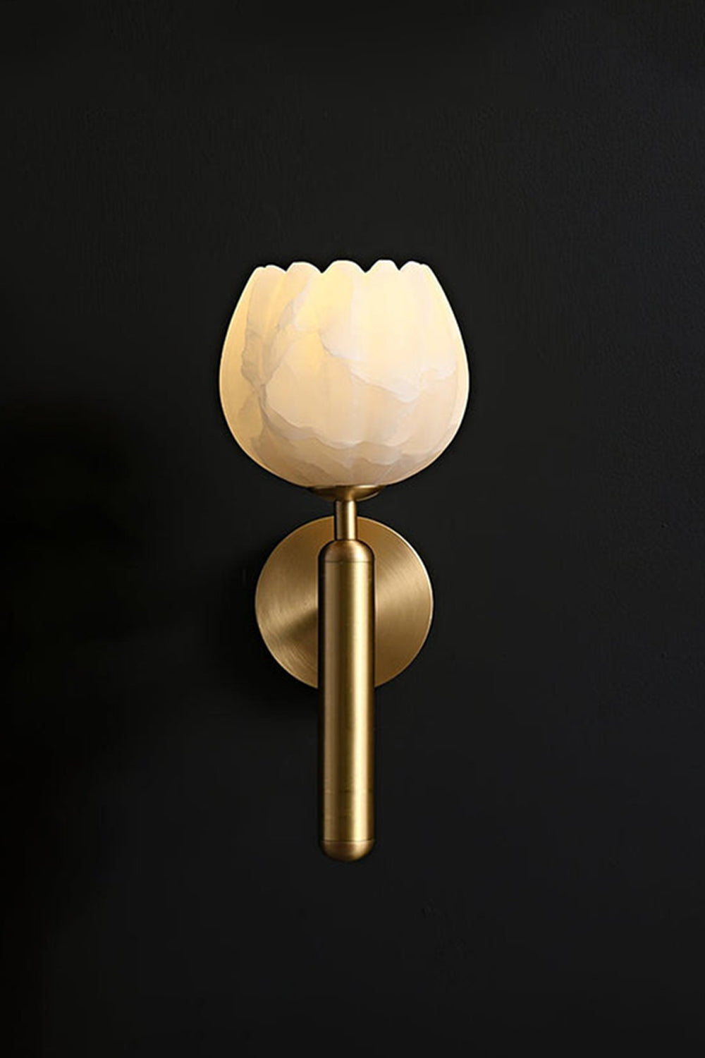 Ondine Alabaster Blossom Wall Sconce | Natural Alabaster and Brass | Minimalist perspective of the brass fixture glowing beautifully on a solid dark black background wall | vexa lamps