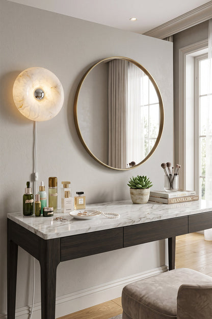Ondine Ring Alabaster Wall Sconce illuminating a modern vanity with a round mirror, cosmetics, and a green plant.
