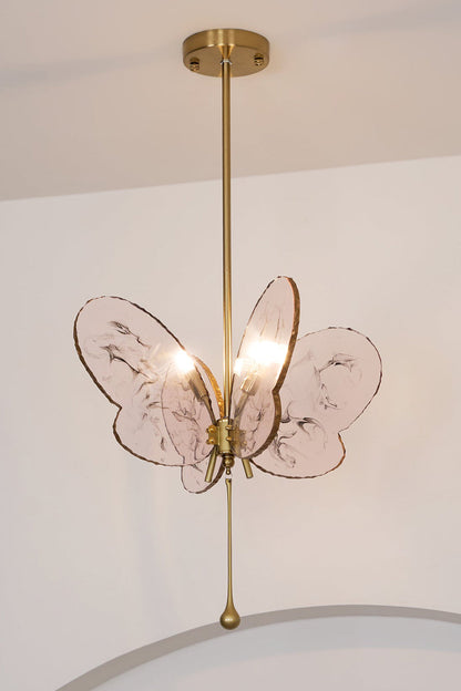 Papillon Glass Butterfly Pendant Lamp | Glass, Metal | Low-angle view looking up at the fully lit pink butterfly hanging light against a plain white wall | vexa lamps