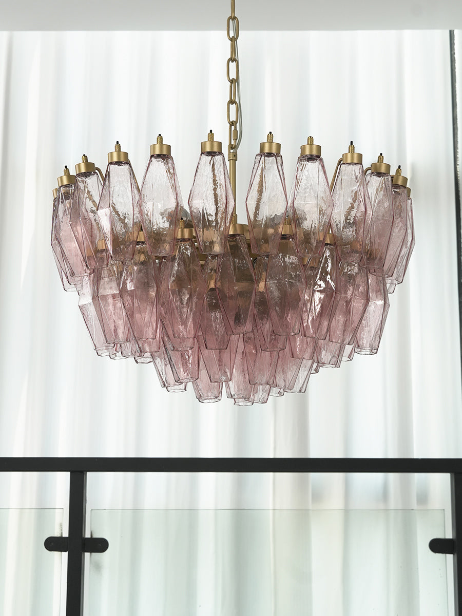 Lit pink glass polyhedron chandelier near a window | Metal, Glass | Close-up showing the warm glowing crystals | vexa lamps