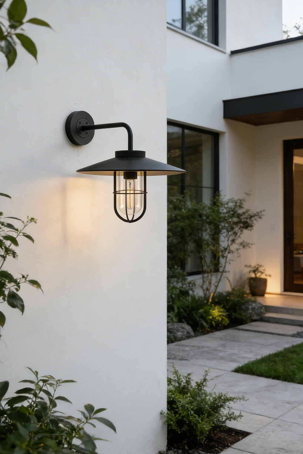 Black Portree wall light lit at night on a house wall | Metal, Glass | Evening exterior shot with garden landscaping | vexa lamps
