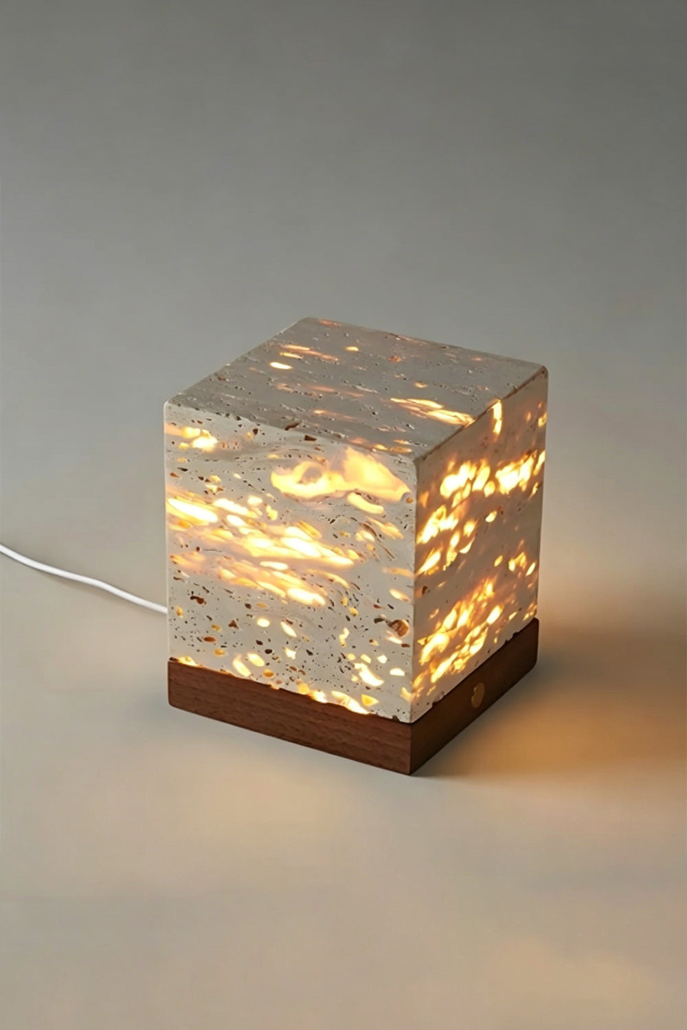 Radiant Monolith Travertine Table Lamp | Travertine, Wood | Lit front view on plain background | Intricate internal light pattern | Dark wood base, gold button | vexa lamps