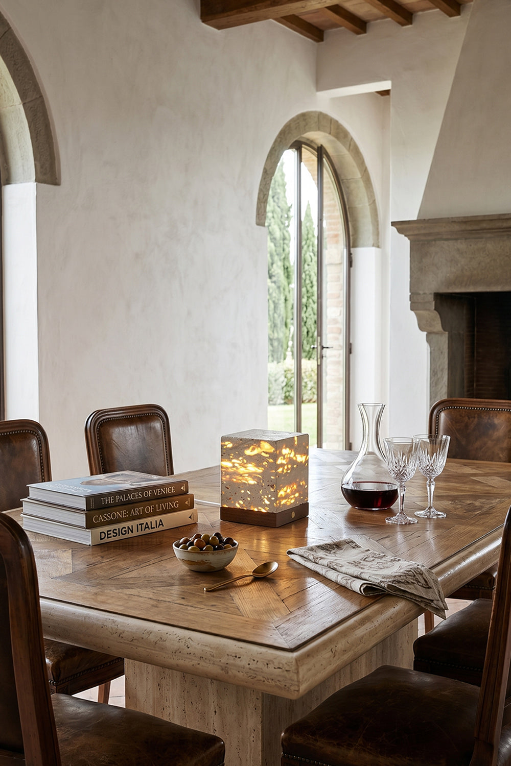 Radiant Monolith Travertine Table Lamp | Travertine, Wood | Lit on travertine dining table | Tuscan-style dining interior | Rustic stone walls, hill view | vexa lamps