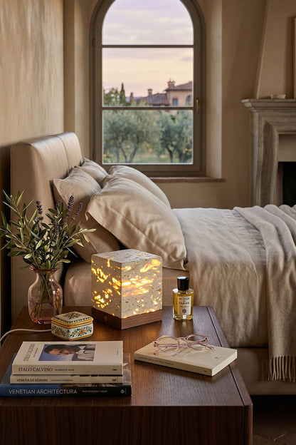 Radiant Monolith Travertine Table Lamp | Travertine, Wood | Lit on wood nightstand | Tuscan bedroom landscape view | Arched window frame, hills | vexa lamps