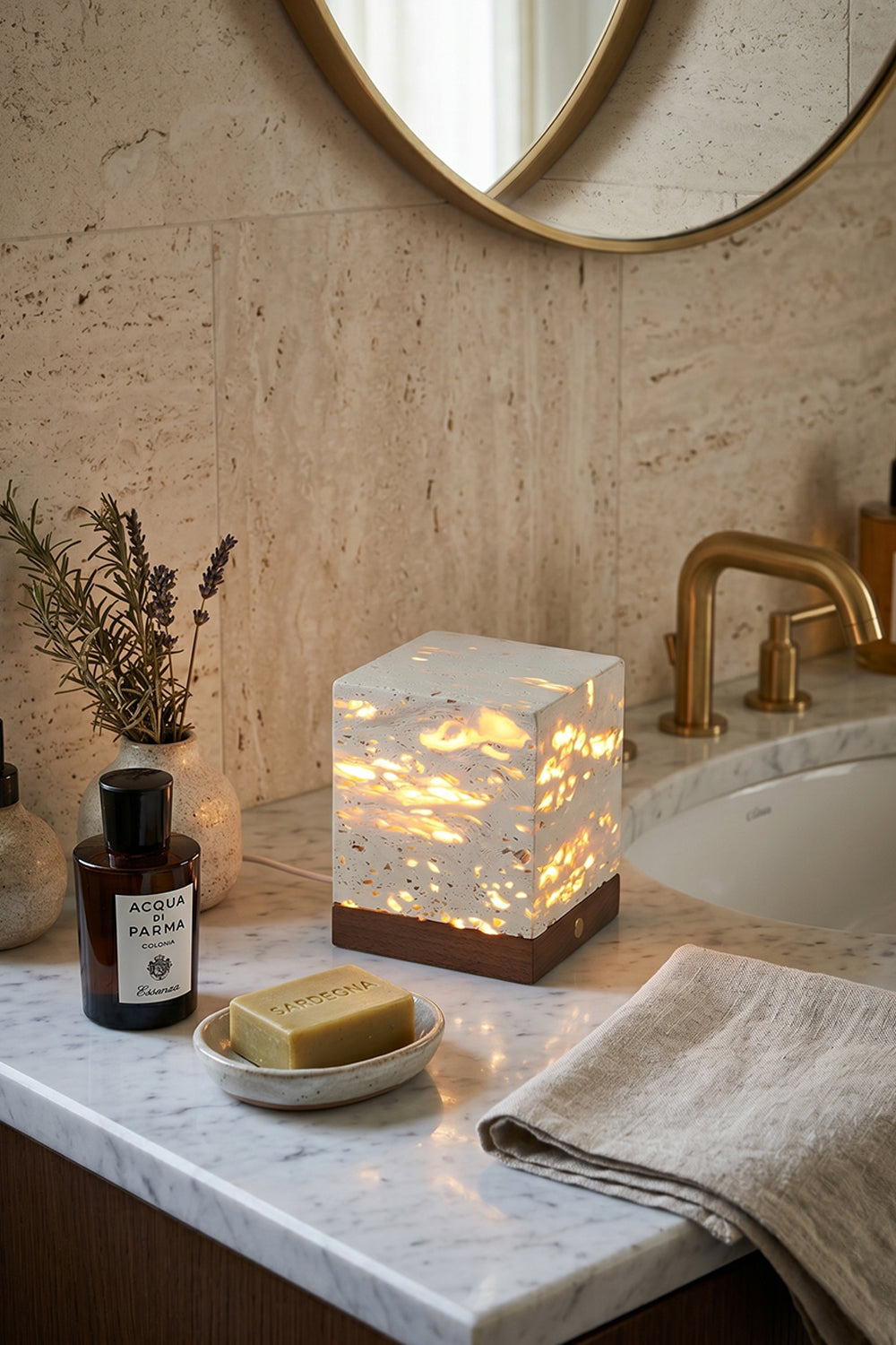 Radiant Monolith Travertine Table Lamp | Travertine, Wood | Unlit on marble vanity | Spa-like bathroom corner | Round mirror, toiletries, towels | vexa lamps
