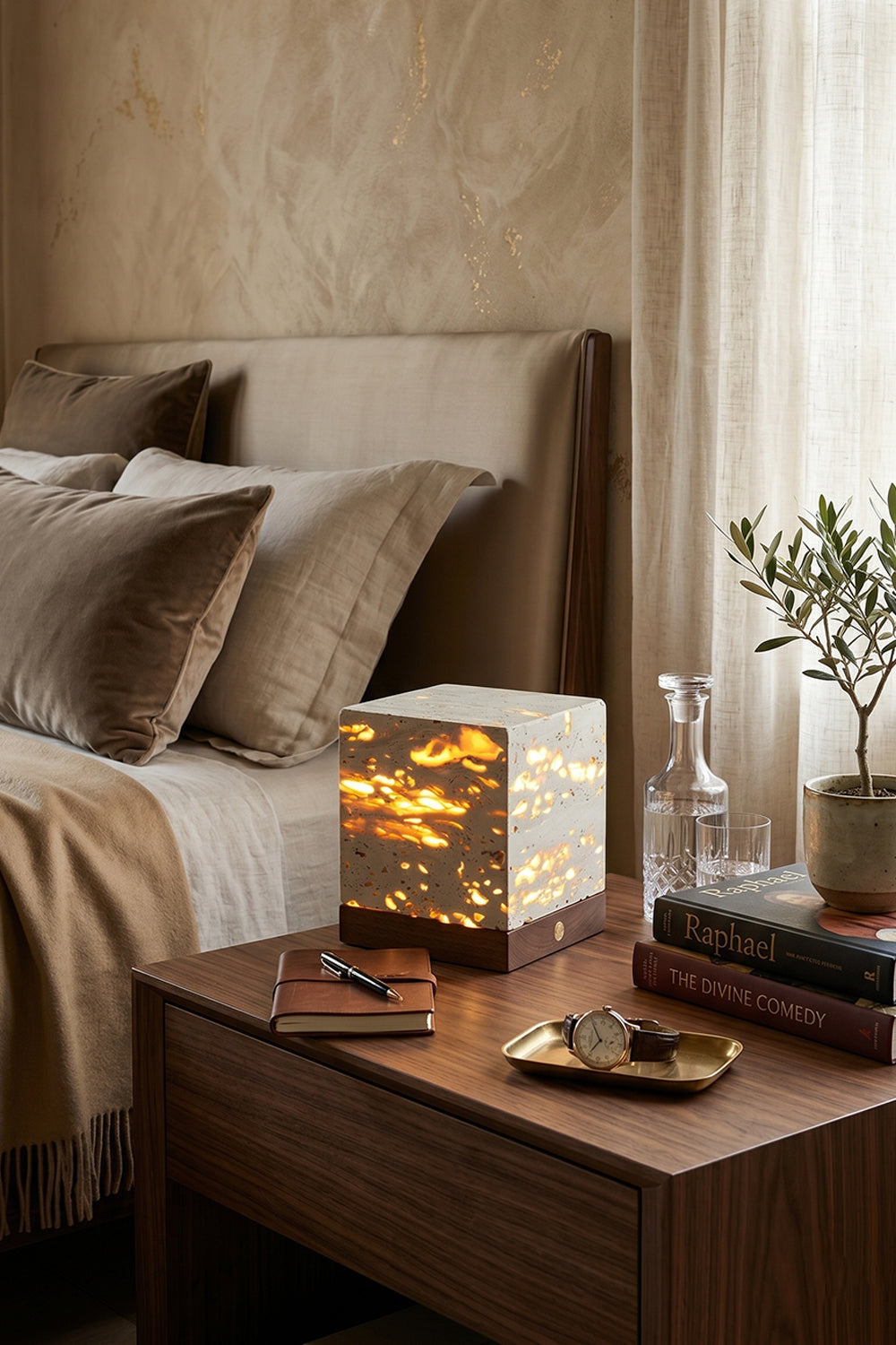 Radiant Monolith Travertine Table Lamp | Travertine, Wood | Lit on dark wood nightstand | Rustic bedroom setting | Textured wall, linen bedding | vexa lamps