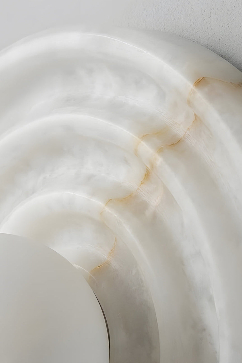 Rhea Rippled Alabaster Wall Sconce | Alabaster Ripple Detail | Close-up focus highlighting the intricate concentric carved ripples and subtle golden-brown mineral veins of the natural white stone | Detail shot | vexa lamps