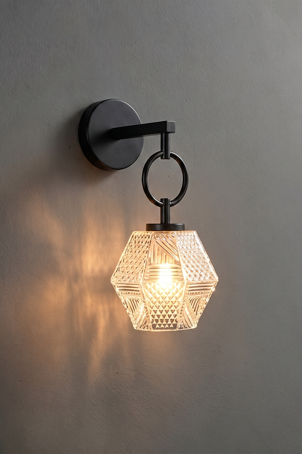 Rosamund Faceted Glass Wall Sconce | Faceted Glass and Black Metal | Matte black finish version illuminated against a dark grey wall | vexa lamps