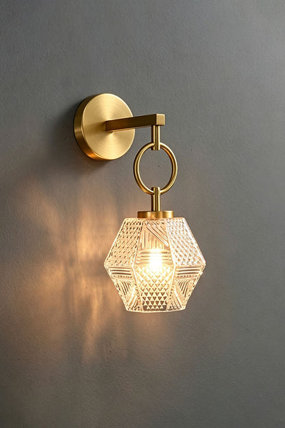 Rosamund Faceted Glass Wall Sconce | Faceted Glass and Brass | Brass finish sconce glowing warmly against a dark grey backdrop | vexa lamps