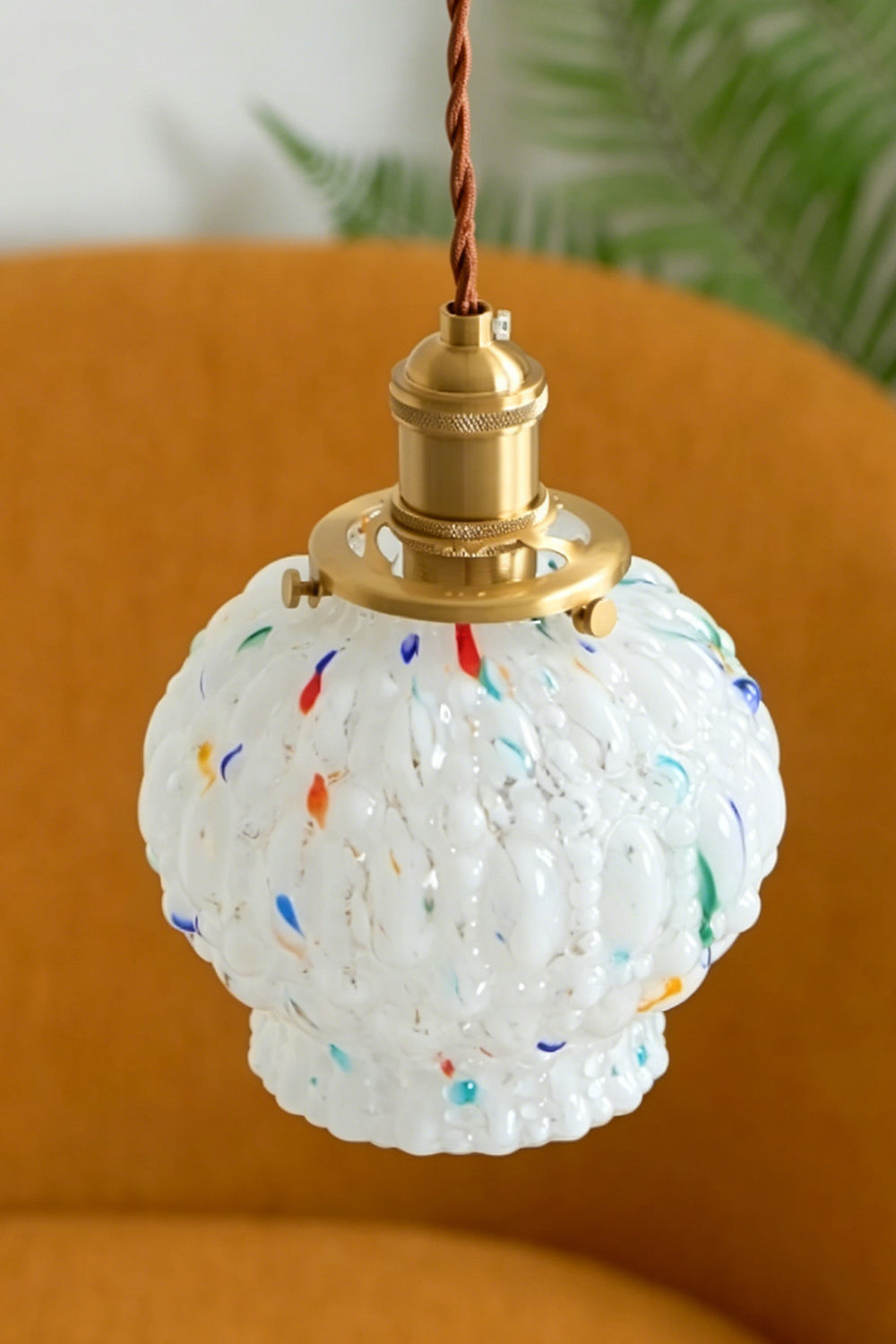 Speckled Bubble Glass Pendant Lamp | Glass, Metal | Frontal view of the unlit white speckled glass pendant hanging elegantly against a warm mustard orange chair backdrop | vexa lamps