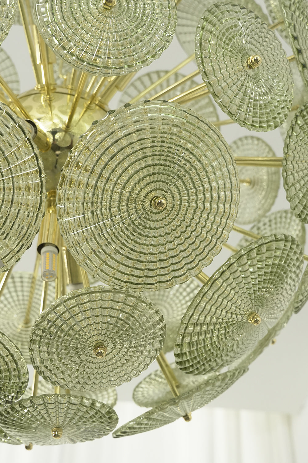 Detailed close-up of unlit green glass sunburst discs | Metal, Glass | Showing texture and brass attachment hooks | vexalamps