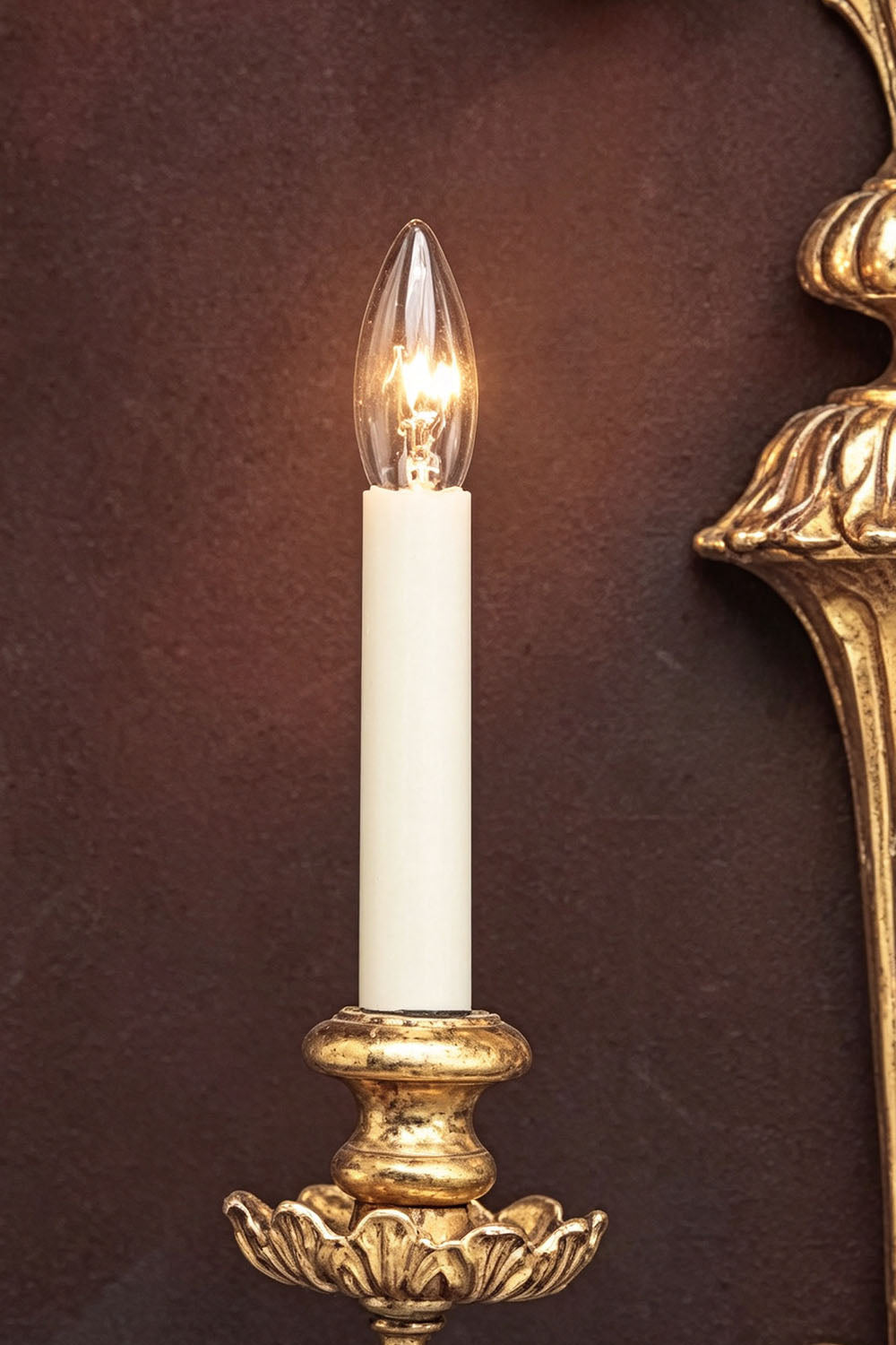 Tamsin Carved Plume Candle Wall Lamp | Carved Resin and Brass | Close-up view of a single candle light glowing against a dark textured background | vexa lamps