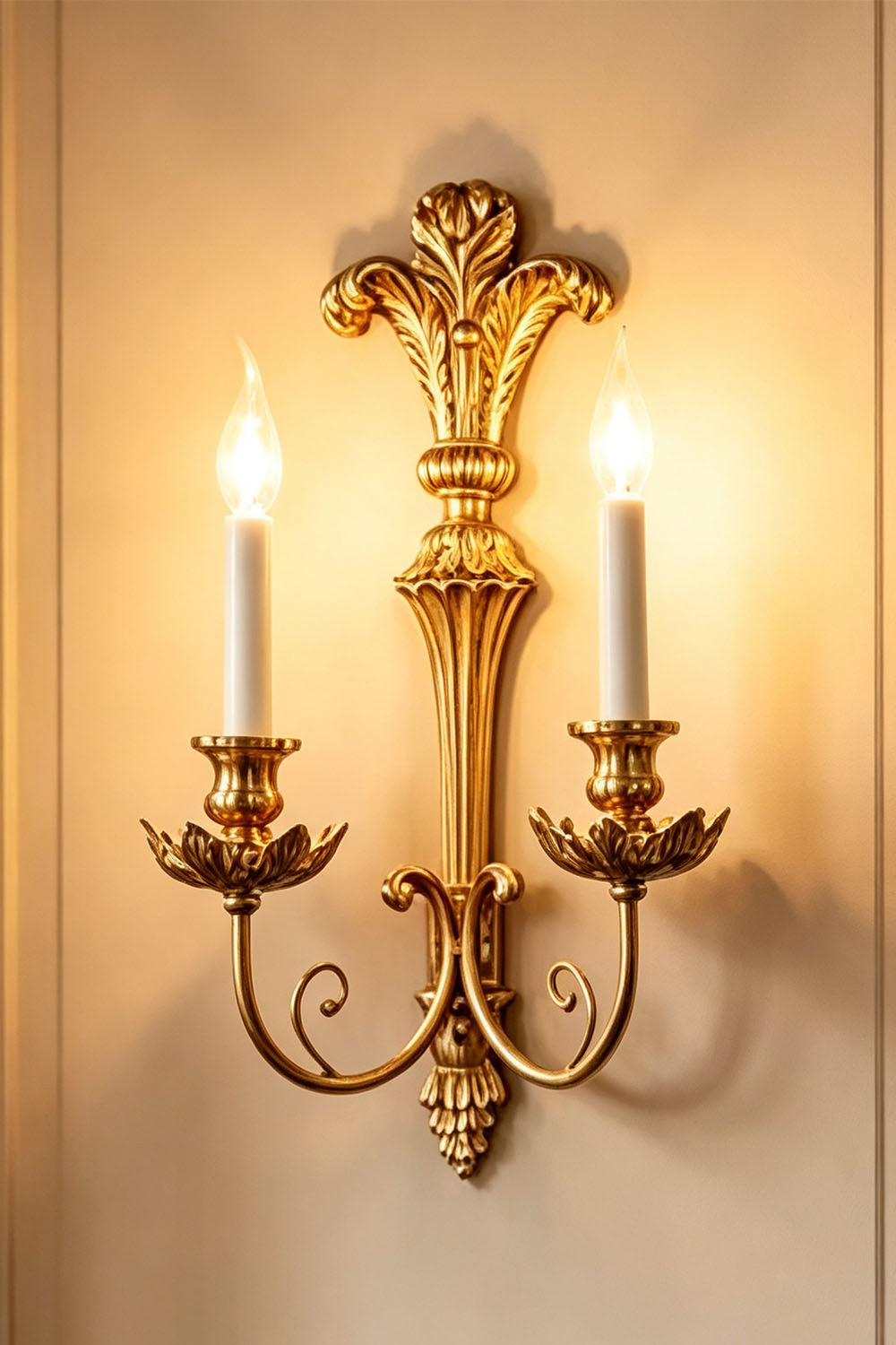 Tamsin Carved Plume Candle Wall Lamp | Carved Resin and Brass | Full view of the double candle sconce glowing warmly on a plain wall | vexa lamps