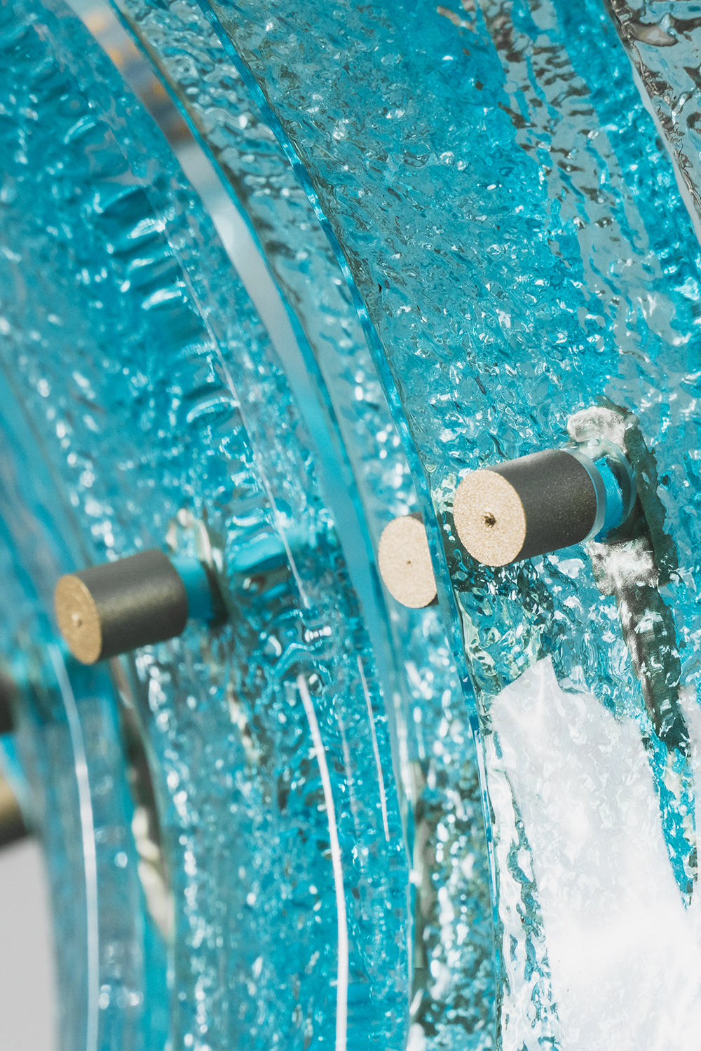 Thalassa Aquamarine Textured Glass Chandelier | Glass, Metal | Macro close-up focus on the thick textured translucent aquamarine glass slats secured tightly by brass bolt hardware screws | Detail shot | vexa lamps