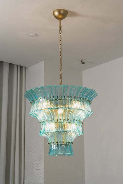 Thalassa Aquamarine Textured Glass Chandelier | Glass, Metal | Alternative studio shot of the illuminated tiered architectural glass light fixture hanging elegantly next to a grey drapery panel | vexa lamps