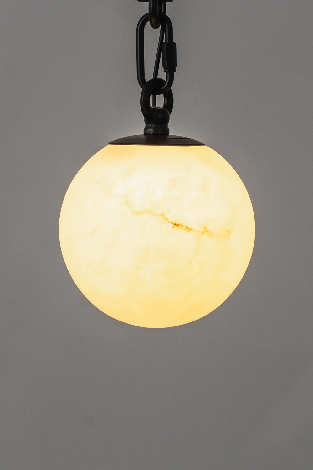 Thalia Alabaster Spherical Chain Chandelier featuring a glowing alabaster sphere on a black chain against a gray background.