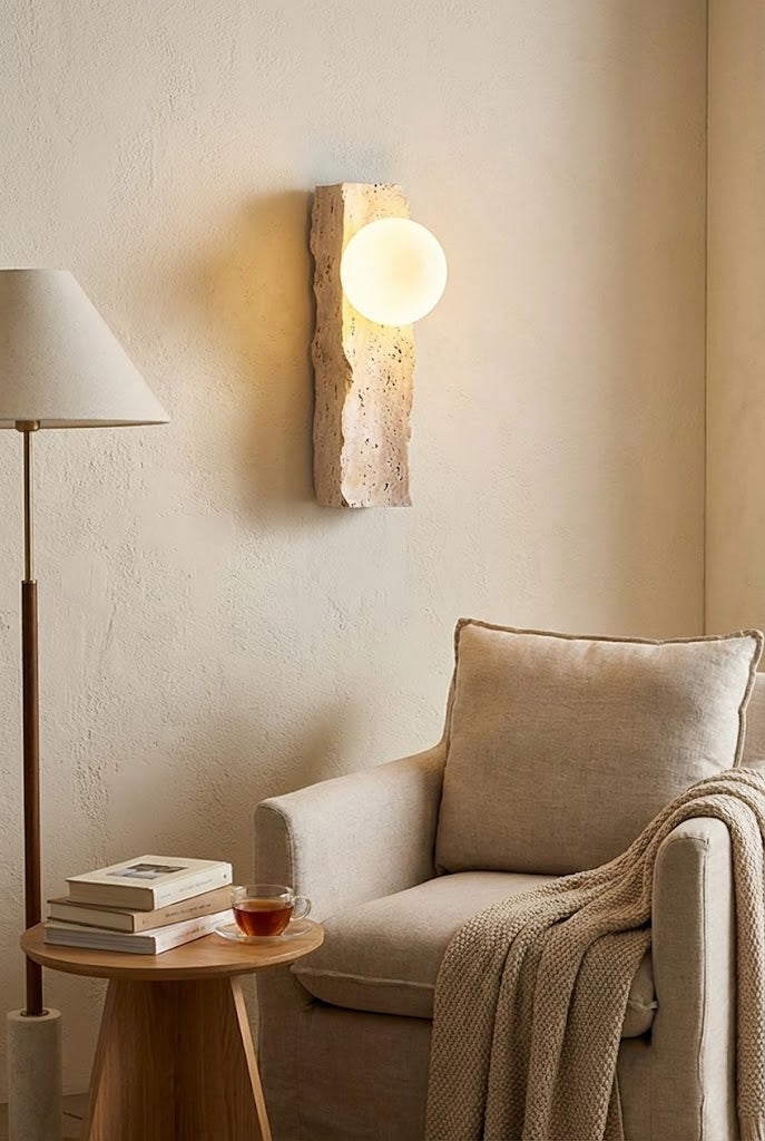 Lit travertine block sconce in a reading nook | Yellow Travertine, Metal, Glass | Mounted above a cozy armchair and floor lamp | vexa lamps