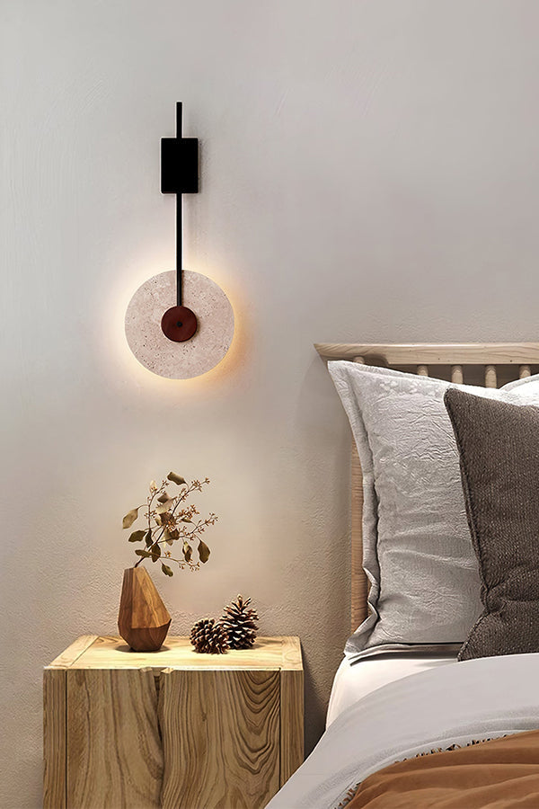 Lit travertine halo sconce over a wooden bedside table | Travertine, Wood, Metal | Cozy bedroom scene with soft textures | vexa lamps